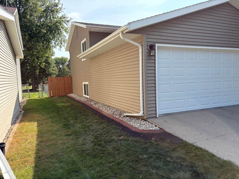 Side view of a house exterior with tan siding, a white garage door, and a gravel flower bed against the foundation.