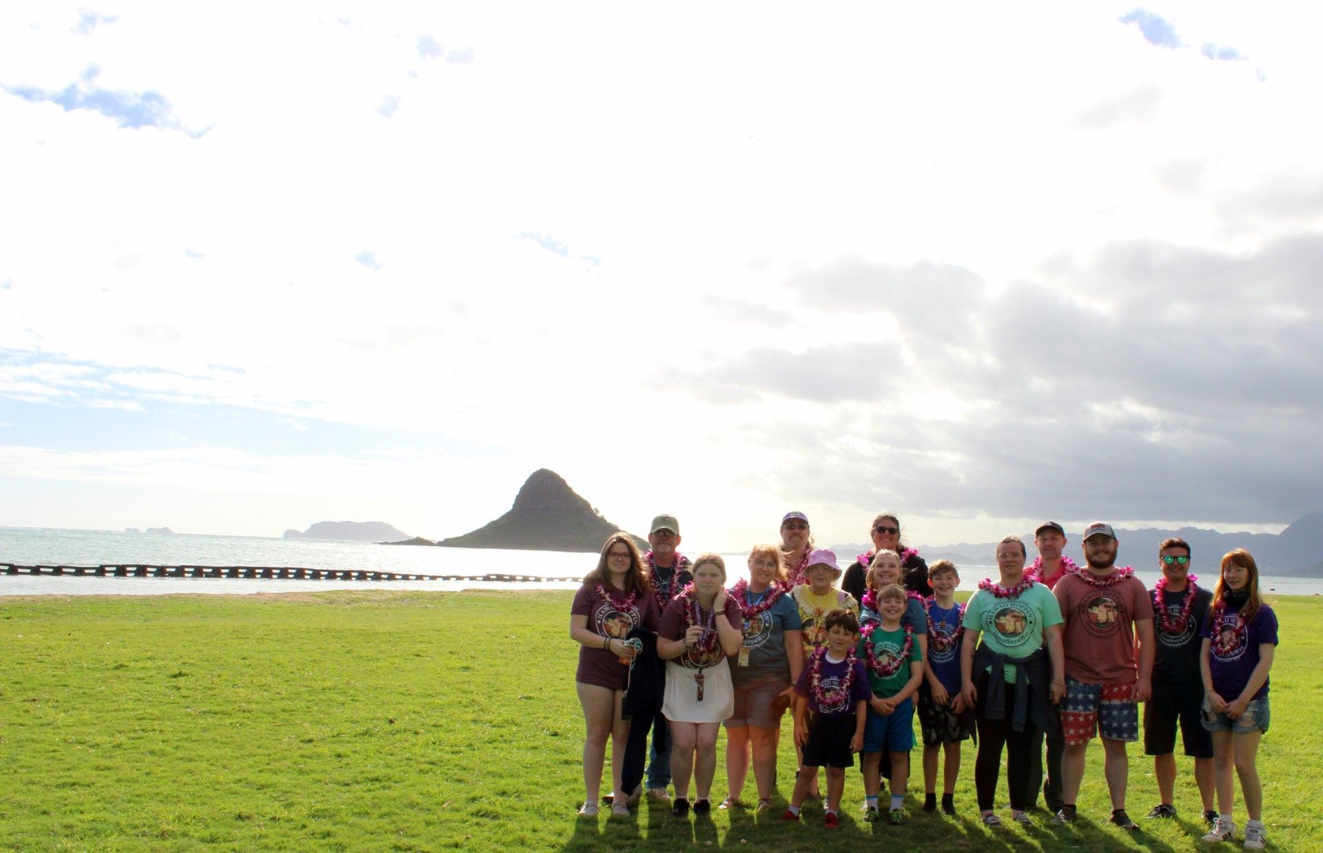 Group of people wearing leis poses in front of a black bus on a sunny day.