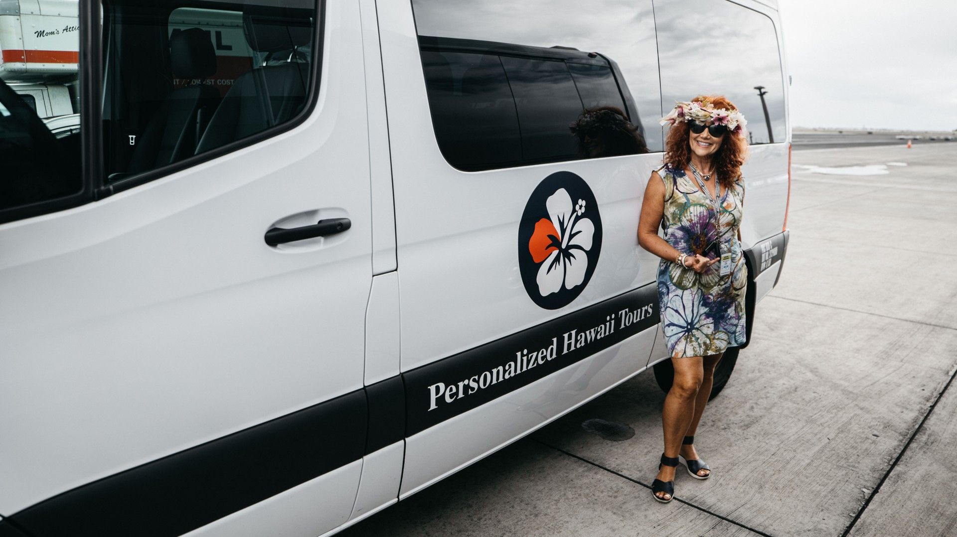 Woman with flower crown next to a white van with logo at an airport.