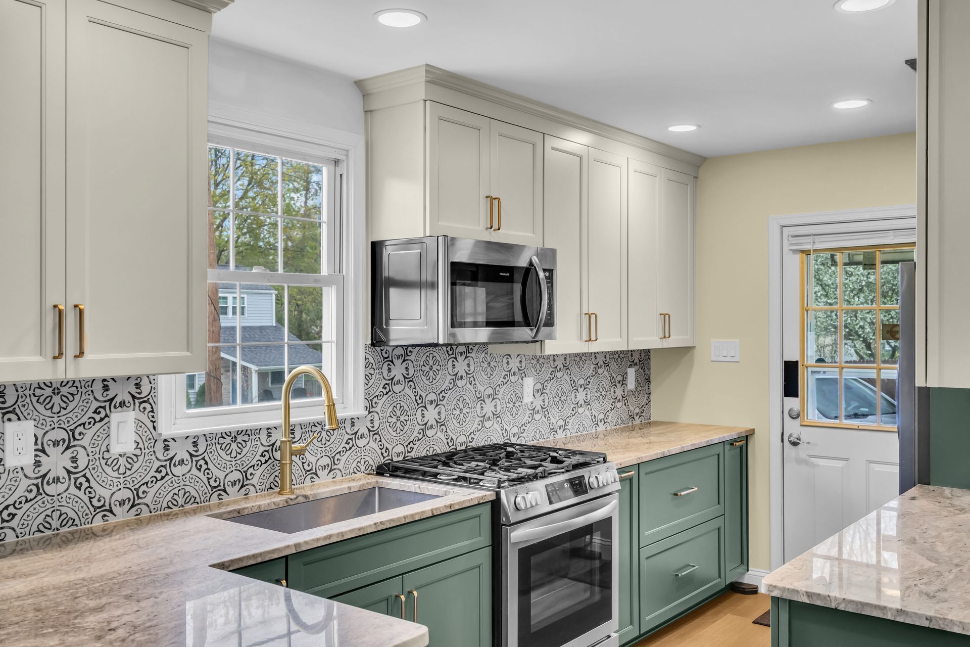 Bright kitchen with white cabinets, green lower cabinets, marble counters, and stainless steel appliances In Bucks Country PA