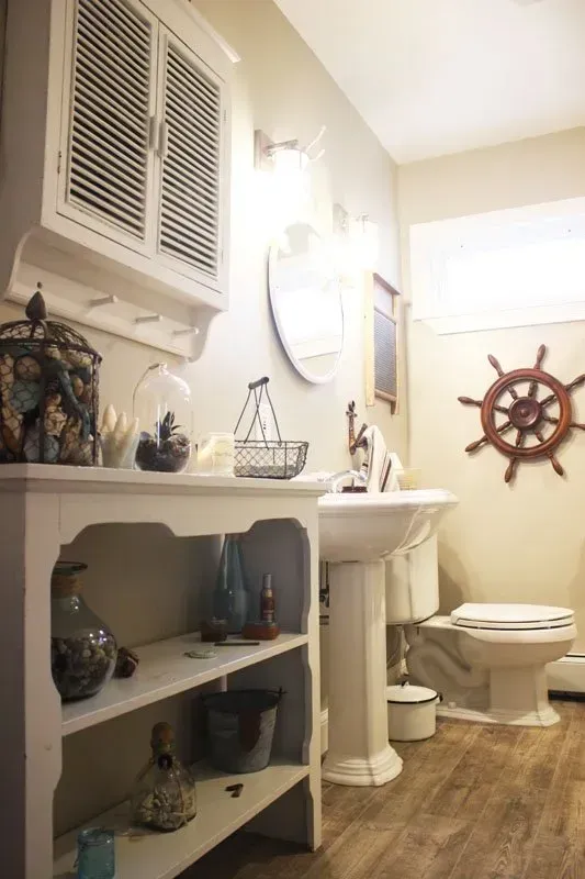 Small bathroom with white sink, toilet, and nautical decor, including a ship’s wheel wall accent In Bucks Country PA