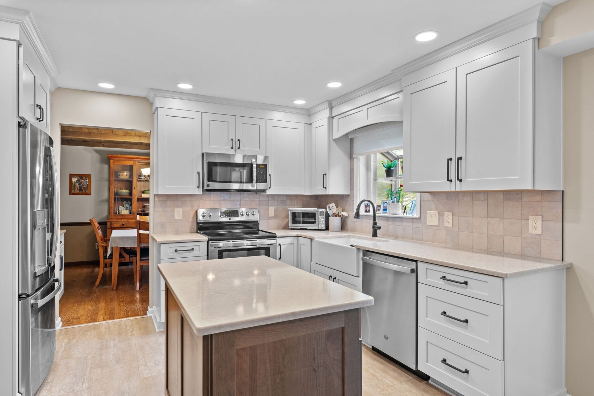 Bright modern kitchen with white cabinets, stainless appliances, island, and beige tile backsplash  In Bucks County PA