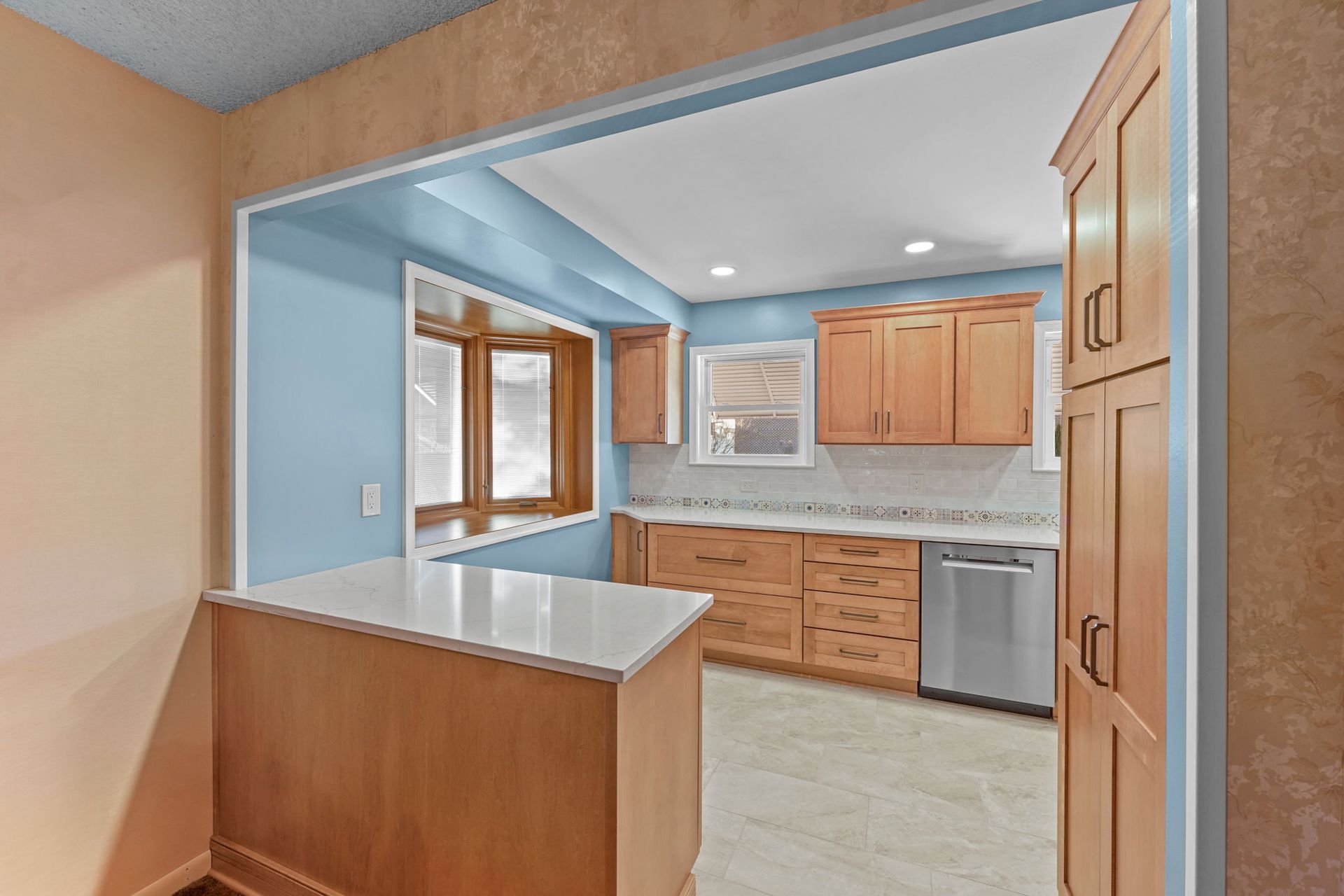 Bright kitchen with light wood cabinets, blue walls, and a breakfast bar opening to a windowed dining area In Bucks County PA