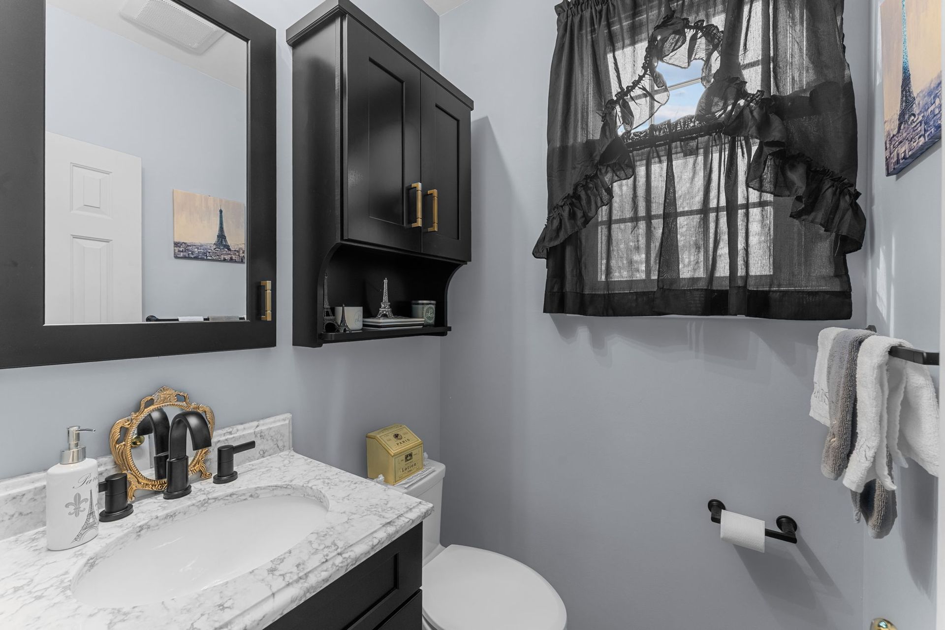 Small gray bathroom with black vanity, white sink, window with black lace curtain, and towel rack  In Bucks County PA