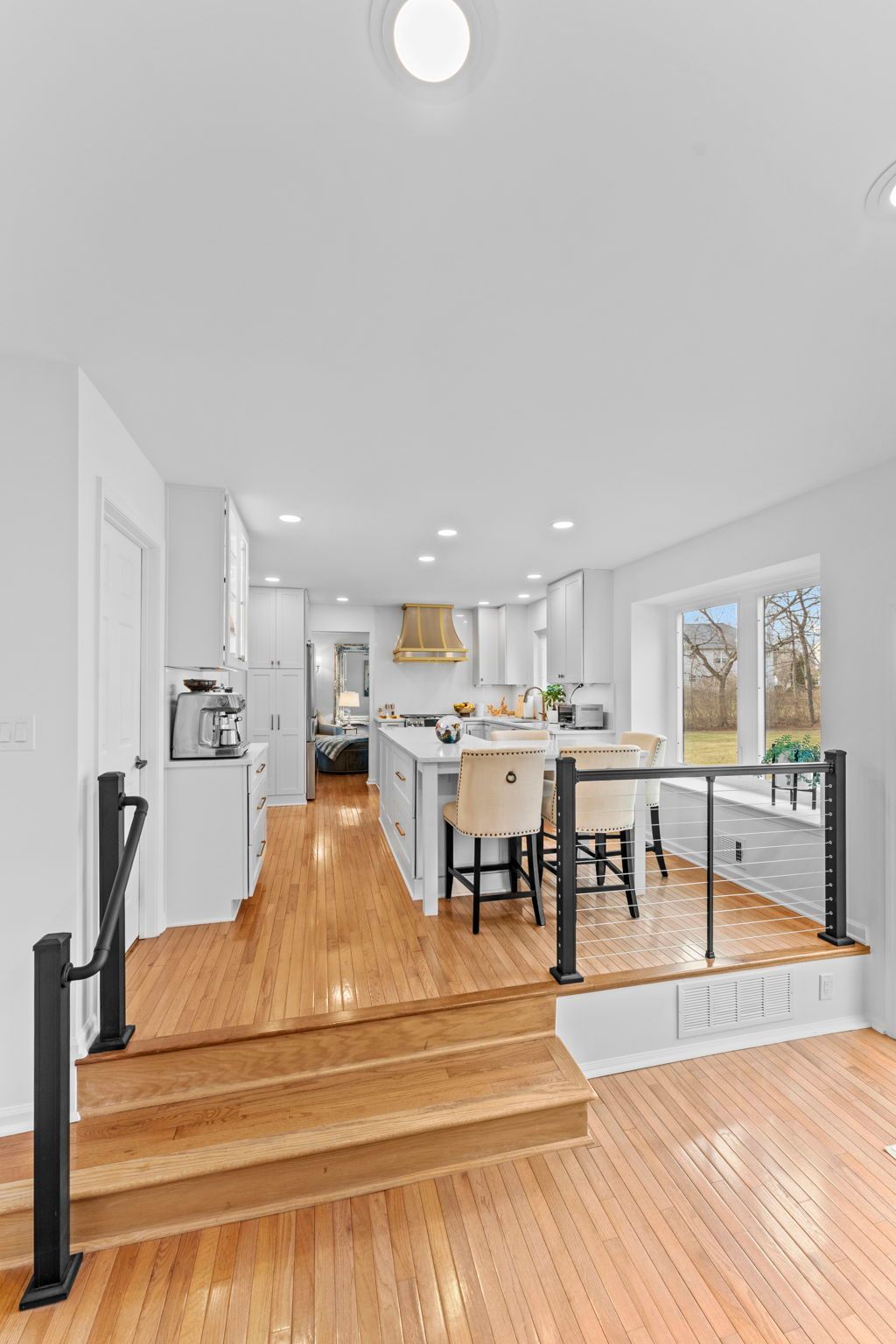 Bright modern kitchen and dining area with wood floors, steps, white walls, and large windows In Bucks Country PA