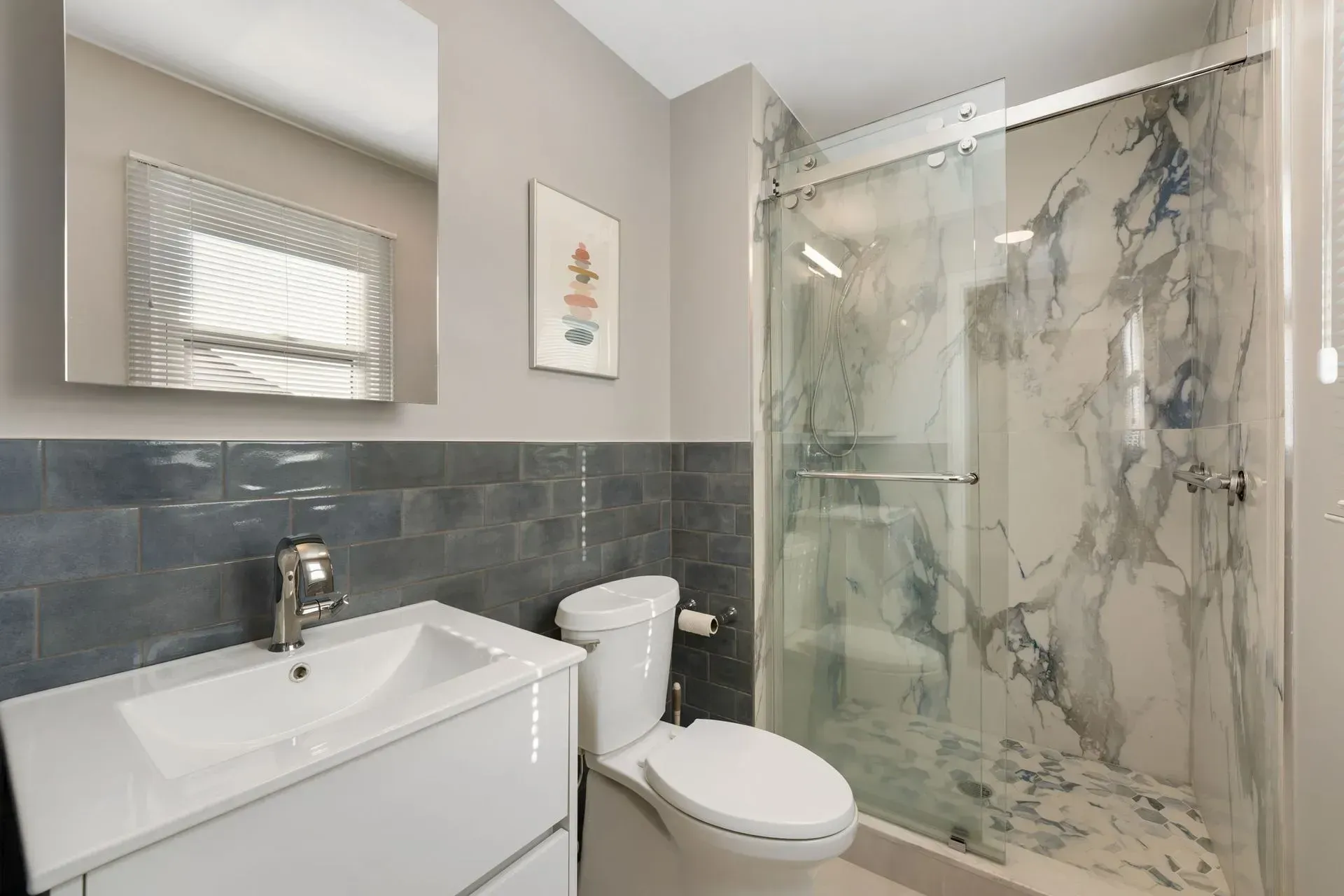 Modern bathroom with white vanity, toilet, gray tile wall, and marble-patterned glass shower enclosure  In Bucks County PA