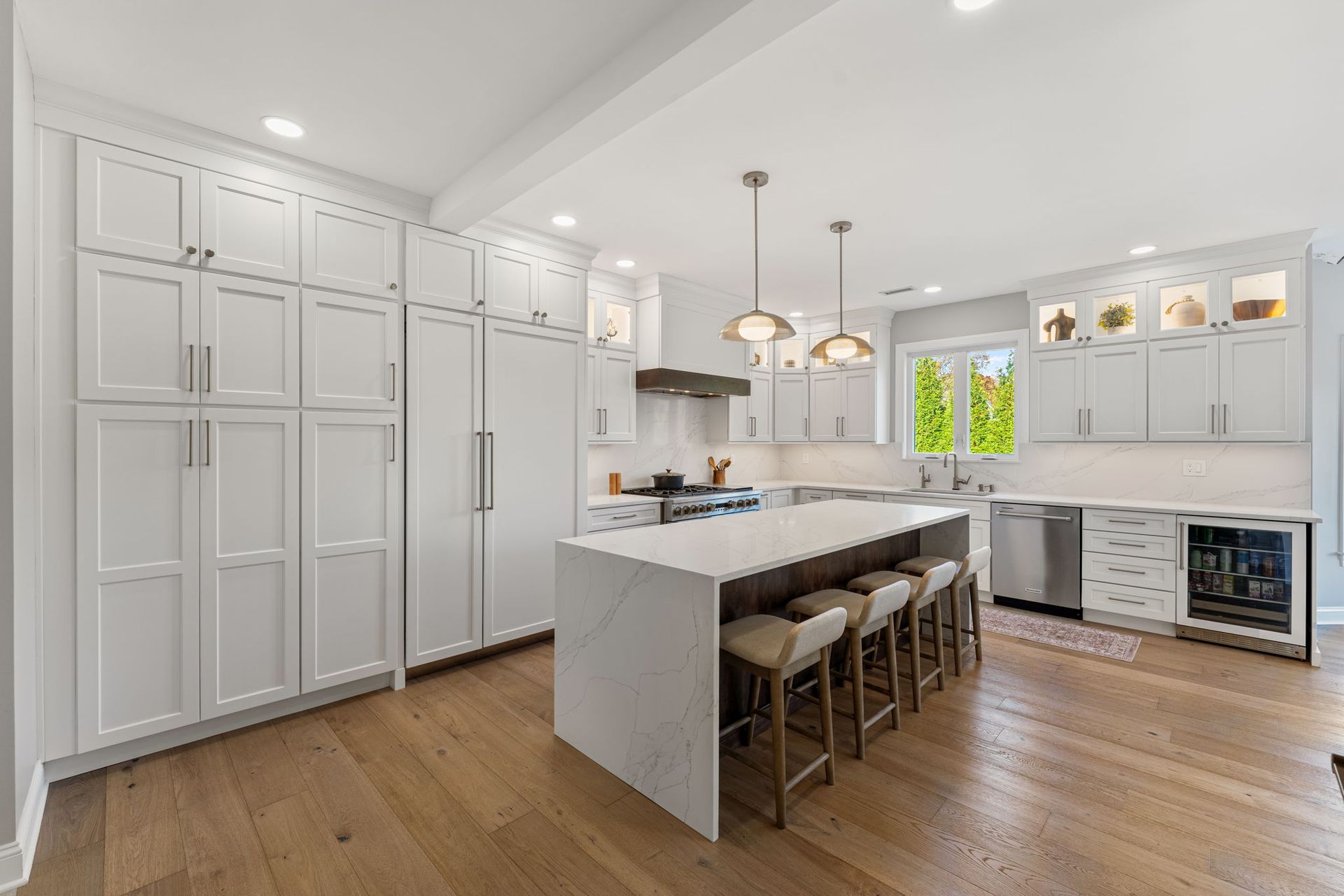 Bright white modern kitchen with large island, bar stools, wood floors, and stainless steel appliances In Bucks Country PA