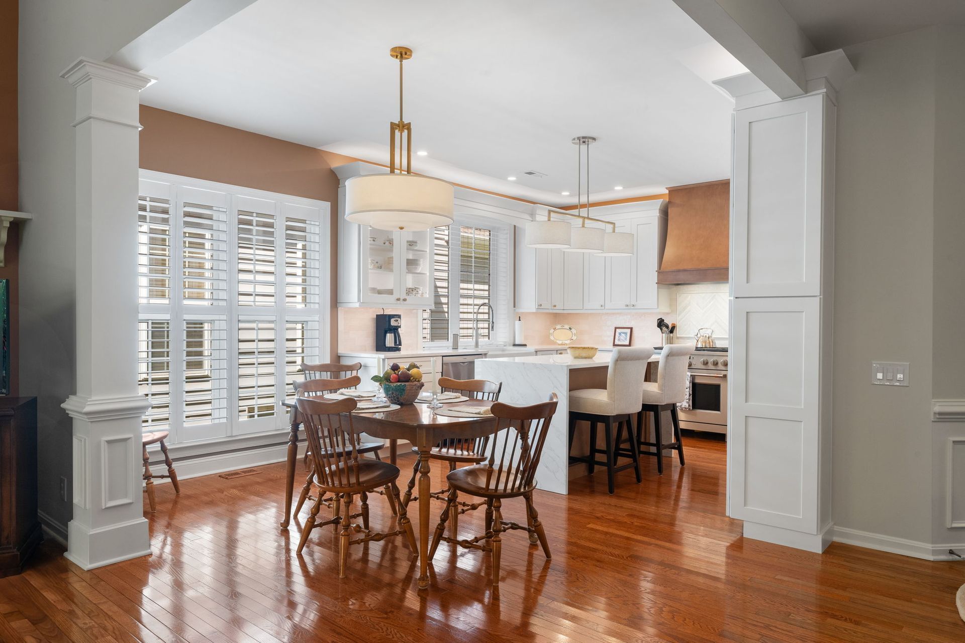 Bright kitchen and dining area with hardwood floors, white cabinets, and a round table by the windows In Bucks County PA