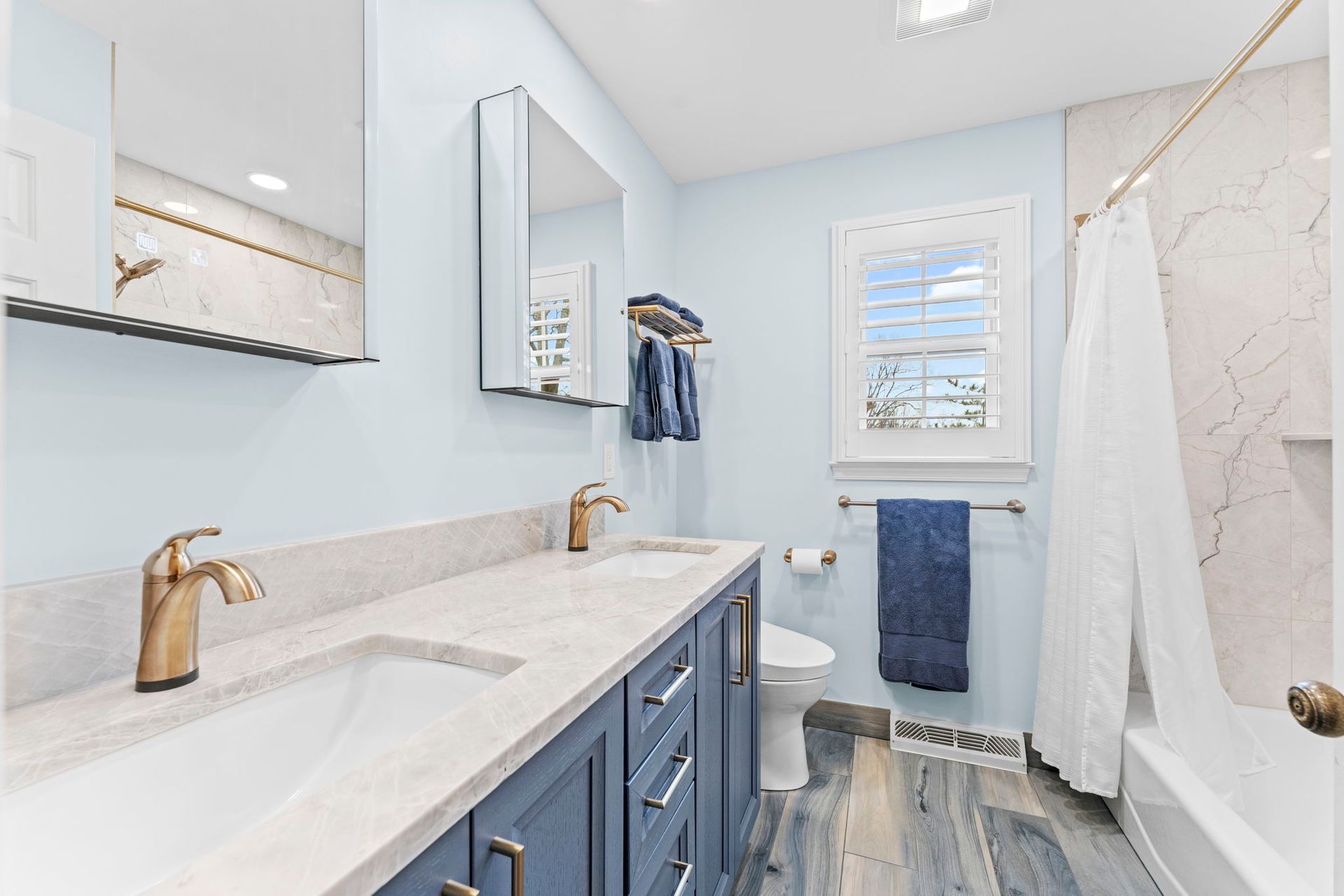 Bright bathroom with blue vanity, marble countertops, mirrors, and white towels on a rack In Bucks County PA