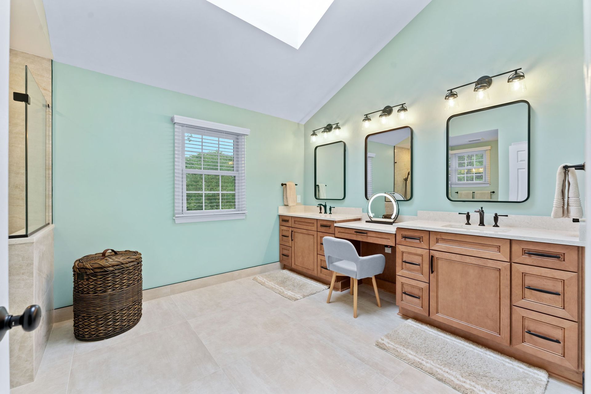 Bright bathroom with mint walls, skylight, double vanity, mirrors, and a wicker hamper In Bucks County PA
