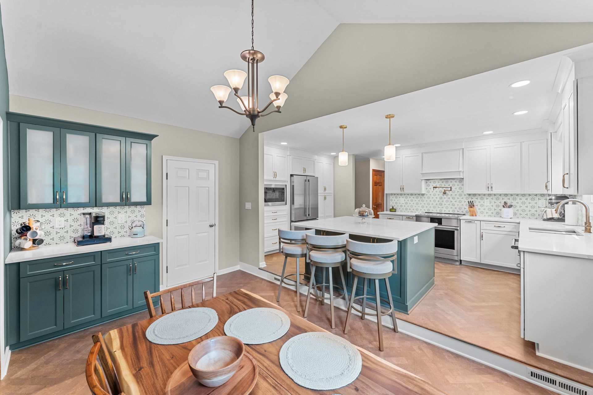 Bright open kitchen with teal cabinets, white island stools, wood floors, and a chandelier In Bucks County PA