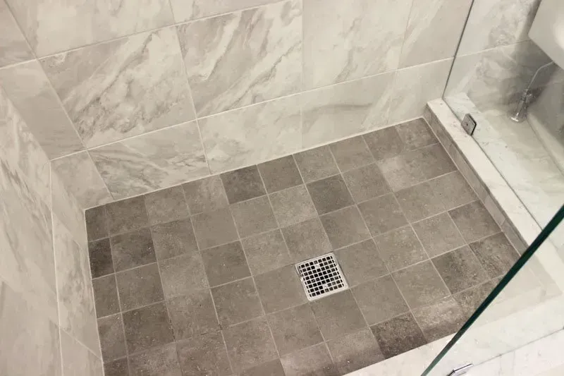 Tiled shower floor with a square drain in the center and glass shower walls In Bucks County PA
