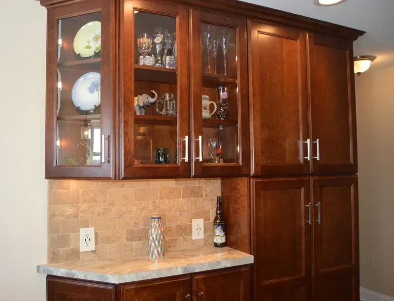 Dark wood kitchen cabinets with glass doors above a beige countertop and backsplash In Bucks County PA