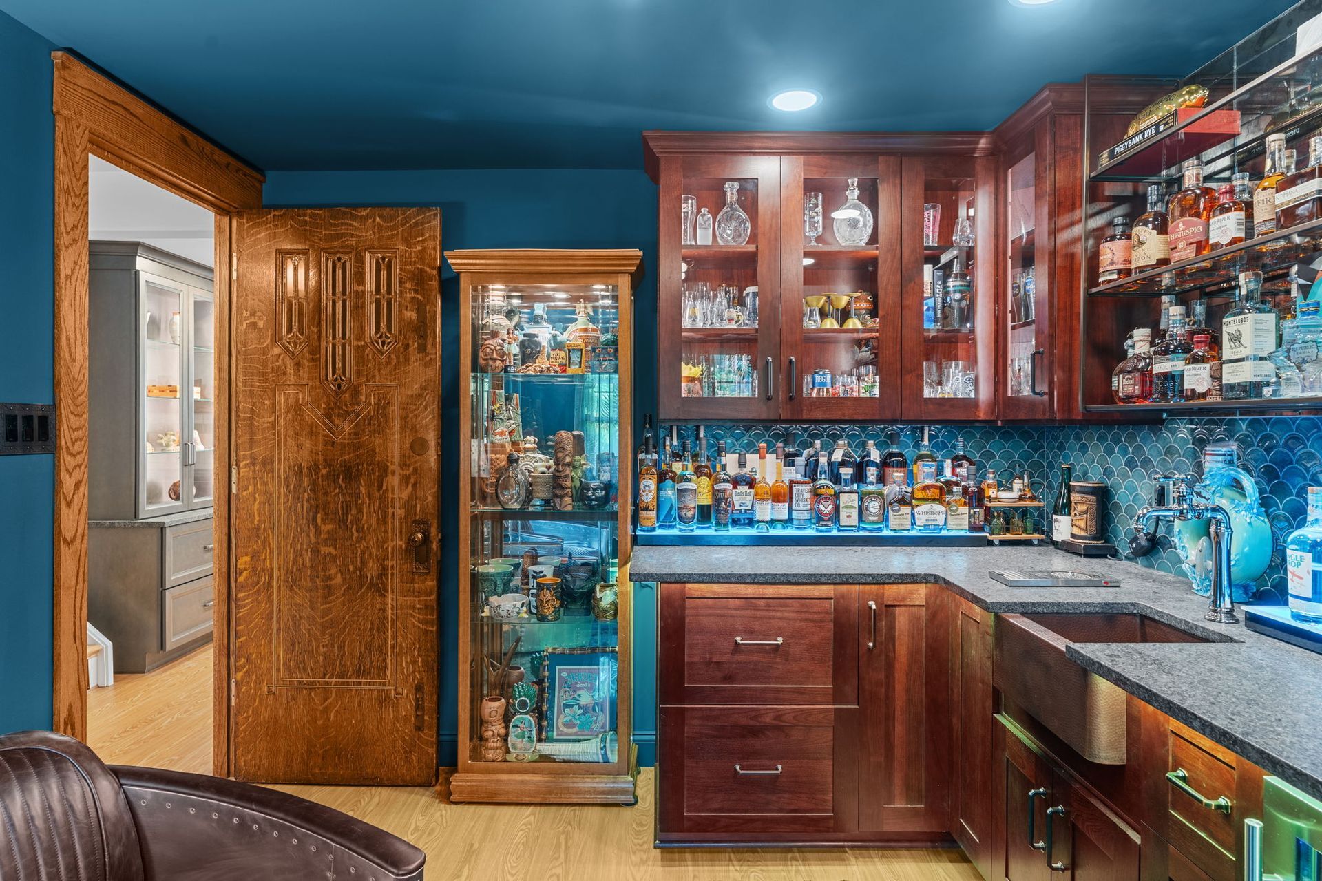 Warm wood home bar with glass cabinets, blue ceiling, mirrored shelves, and a glass-door drink fridge In Bucks County PA