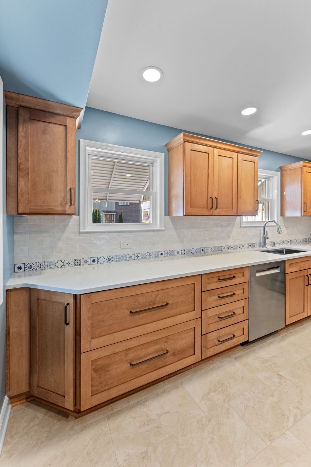 Modern kitchen with light wood cabinets, white countertops, blue walls, and recessed ceiling lights In Bucks County PA