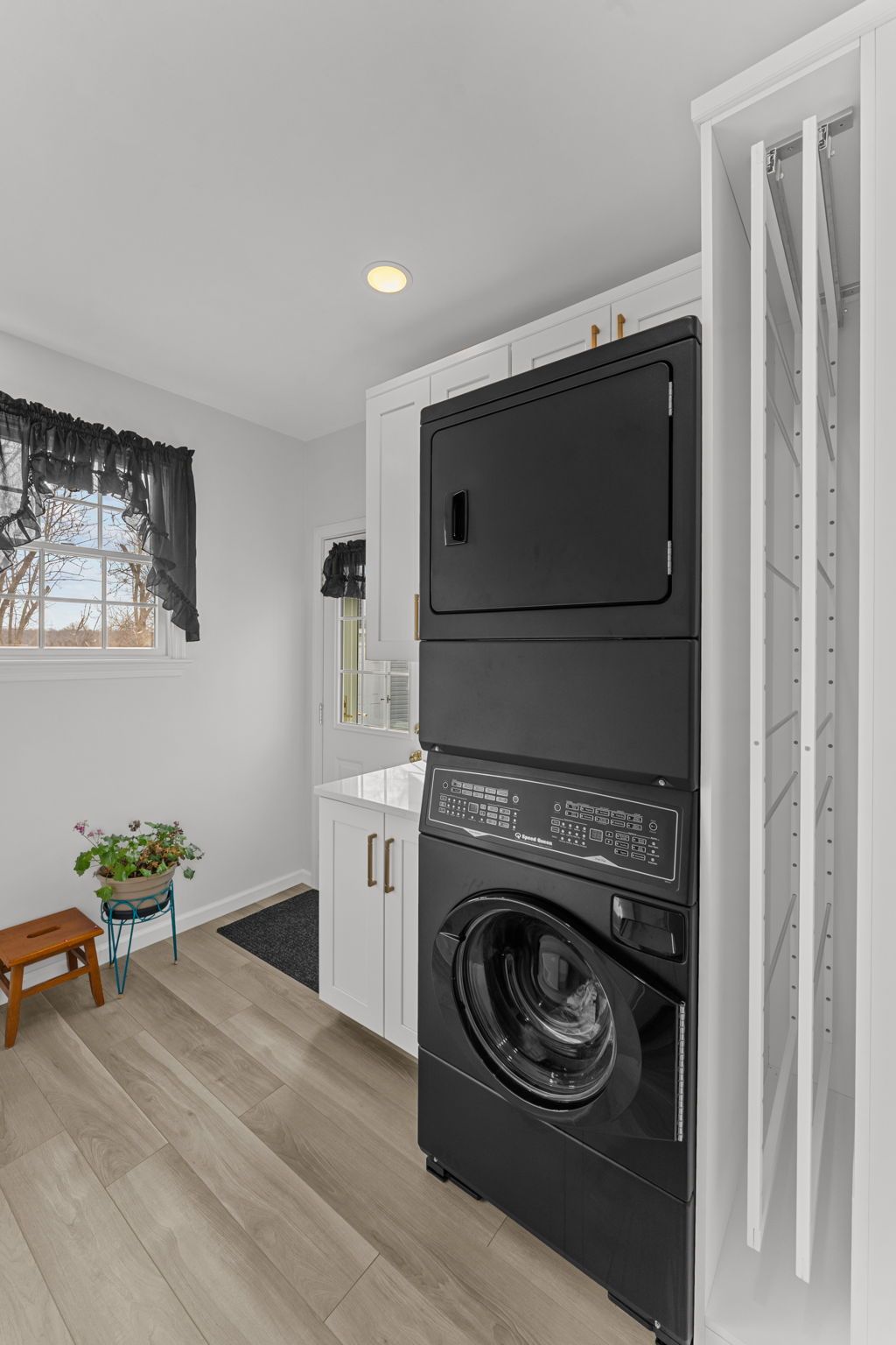 Laundry room with stacked black washer and dryer beside a white sink and window In Bucks County PA