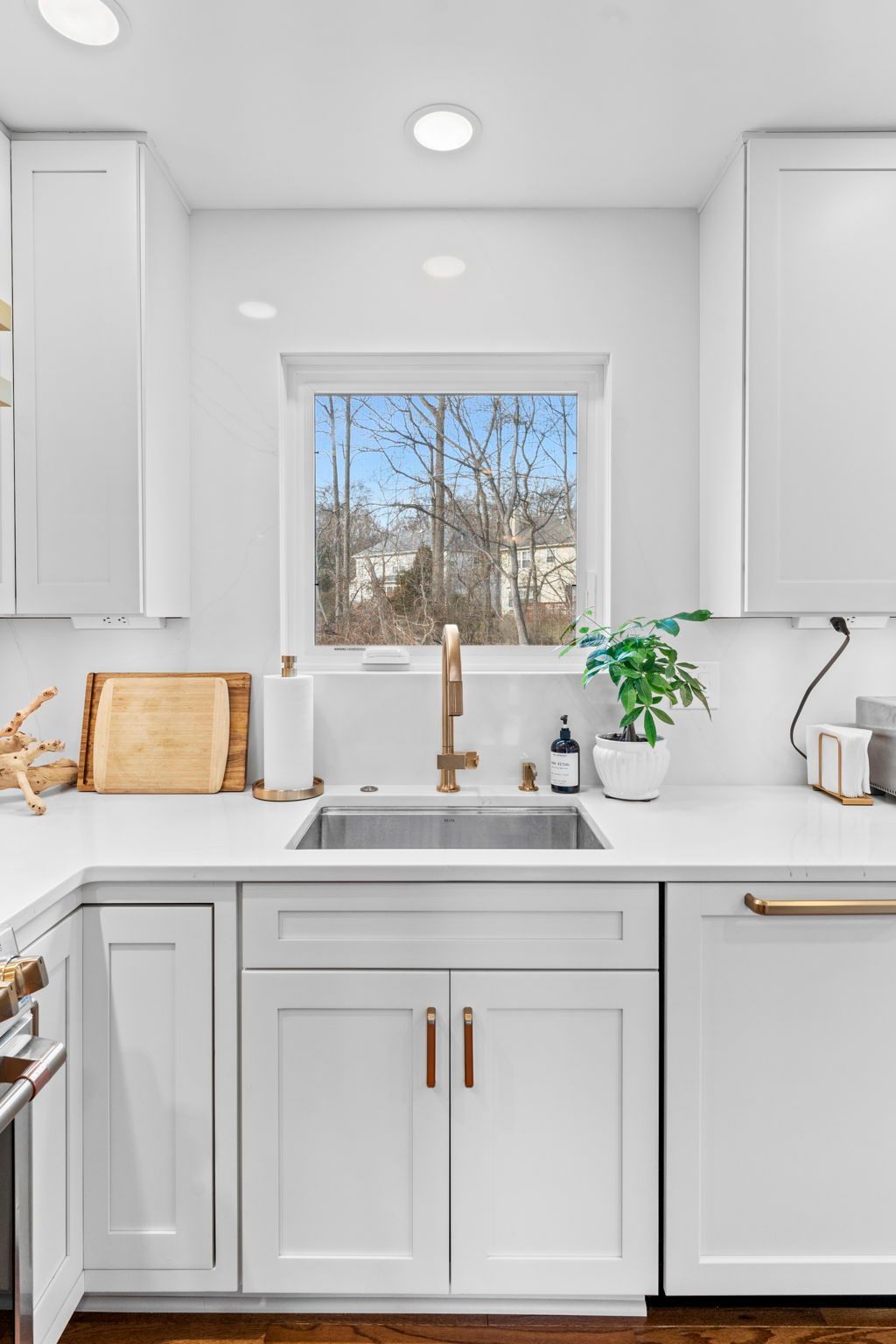 Bright white kitchen with sink under a window, brass faucet, and potted plant on the counter In Bucks Country PA