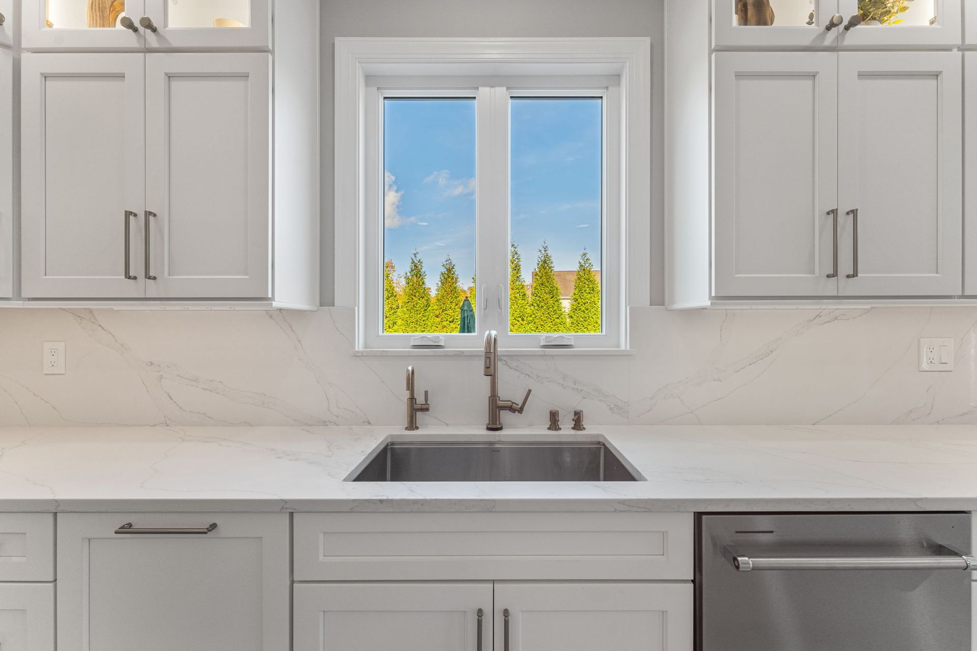 Modern white kitchen with a sink beneath a window and light gray cabinets In Bucks Country PA