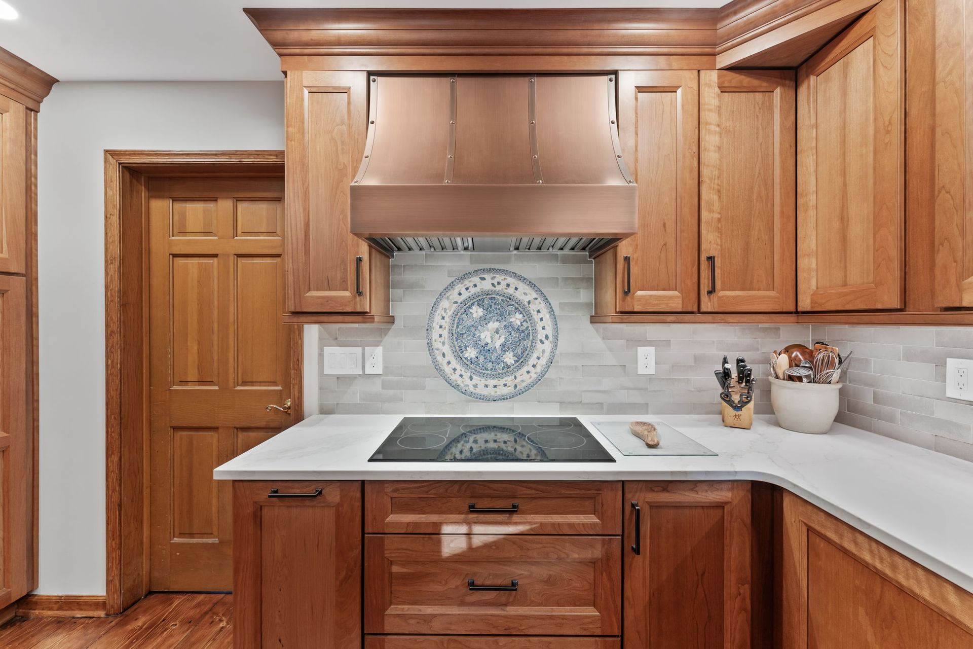 Wooden kitchen with white countertops, stainless stove, and decorative blue-and-white tile backsplash In Bucks County PA