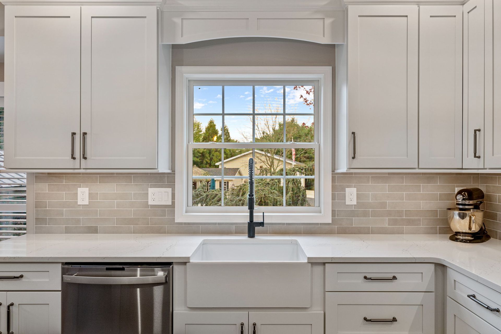 Modern white kitchen with farmhouse sink, window view, and light wood cabinets  In Bucks County PA