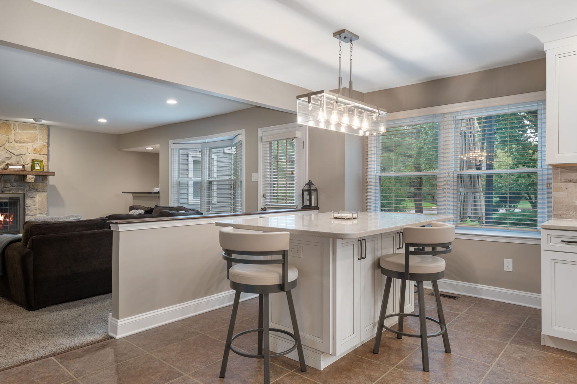 Bright modern kitchen with white island, two stools, chandelier, and large windows In Bucks County PA