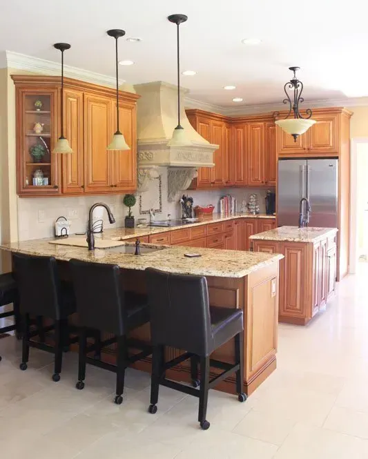 Bright kitchen with granite island, wooden cabinets, stainless fridge, and three black barstools  In Bucks County PA