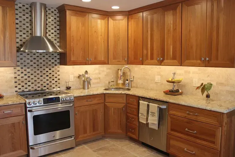 Modern kitchen with wood cabinets, stainless stove, tile backsplash, and beige countertops In Bucks Country PA