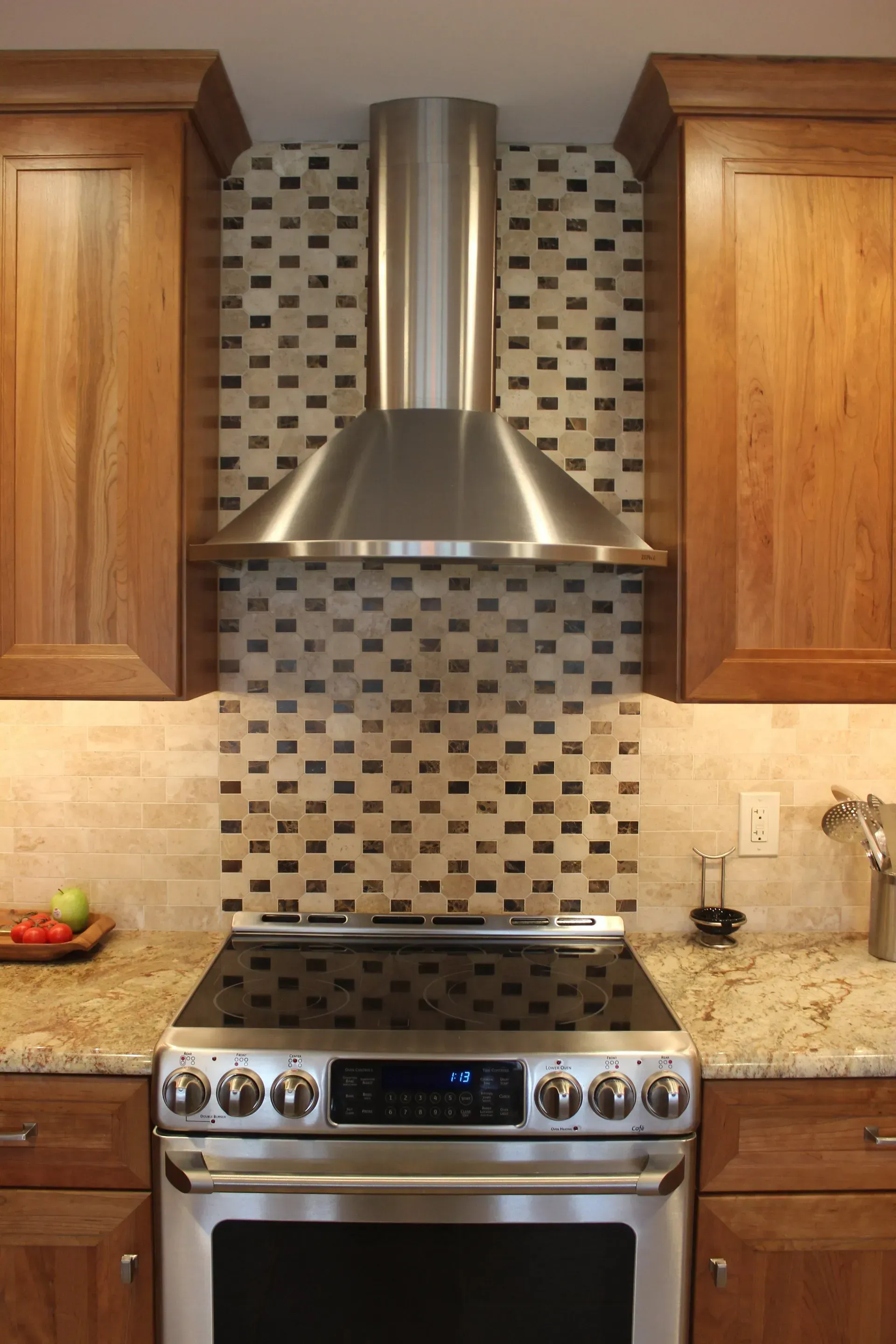 Modern kitchen with stainless steel range and hood between wood cabinets and mosaic tile backsplash In Richboro PA