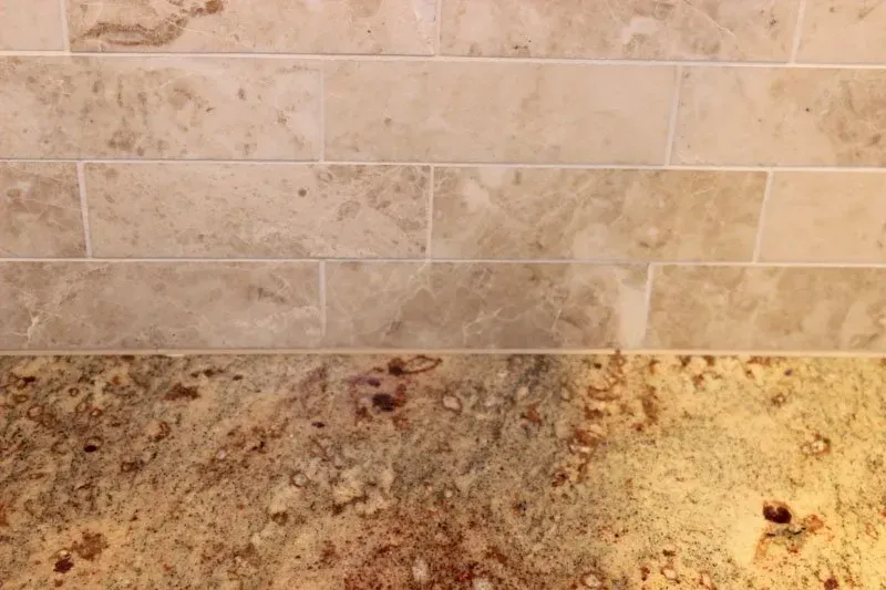 Beige tiled backsplash above a speckled granite countertop with a few dark stains In Richboro PA