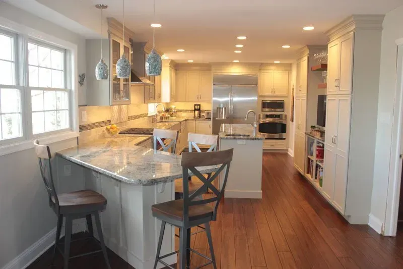 Bright, modern kitchen with white cabinets, marble island, bar stools, and hardwood floors In Bucks County PA