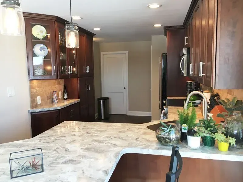 Modern kitchen with dark wood cabinets, marble island, pendant lights, and a vase of flowers on the counter In Bucks County PA