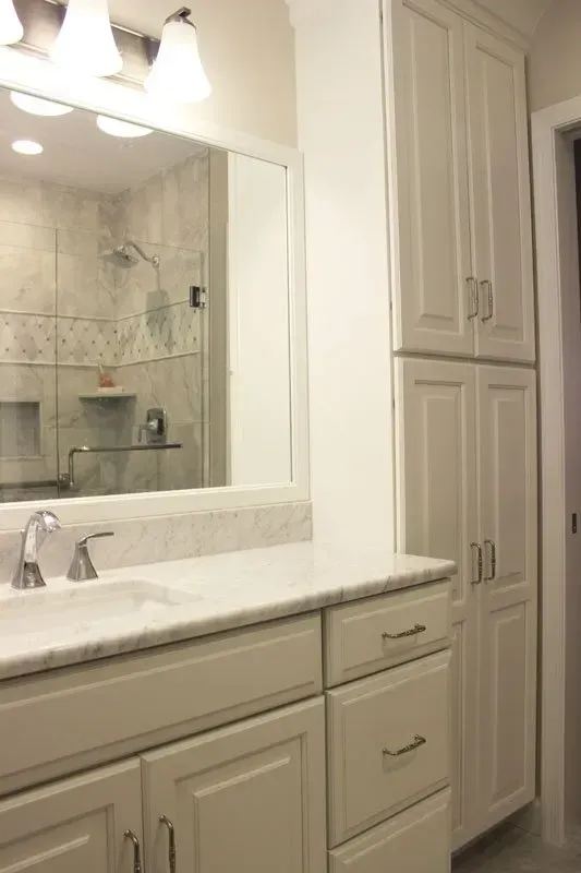 Bathroom vanity with white cabinets, marble countertop, large mirror, and built-in storage tower  In Bucks County PA
