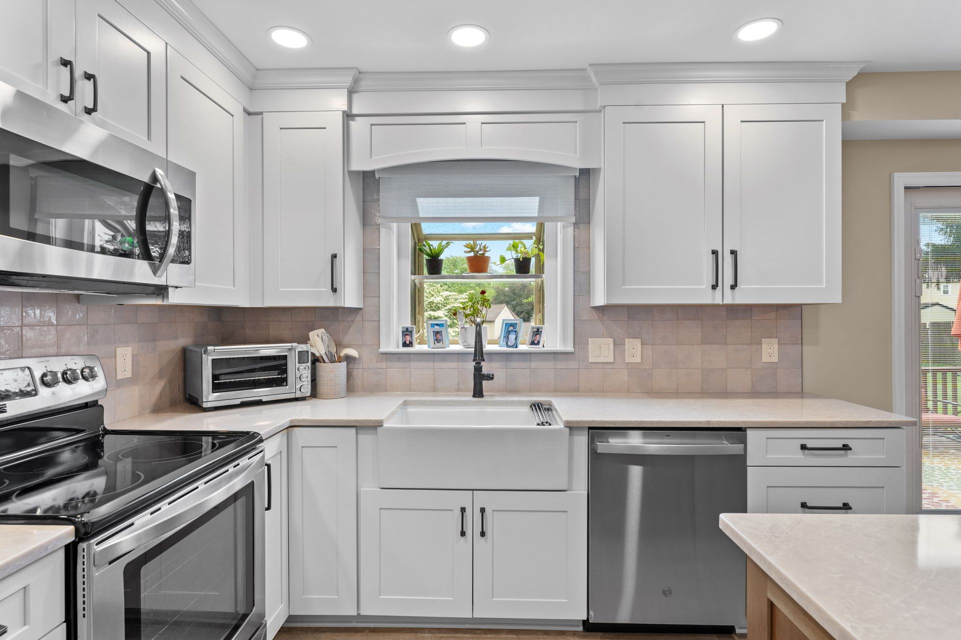 Bright white kitchen with stainless appliances, a sink under a window, and a light beige backsplash  In Bucks County PA
