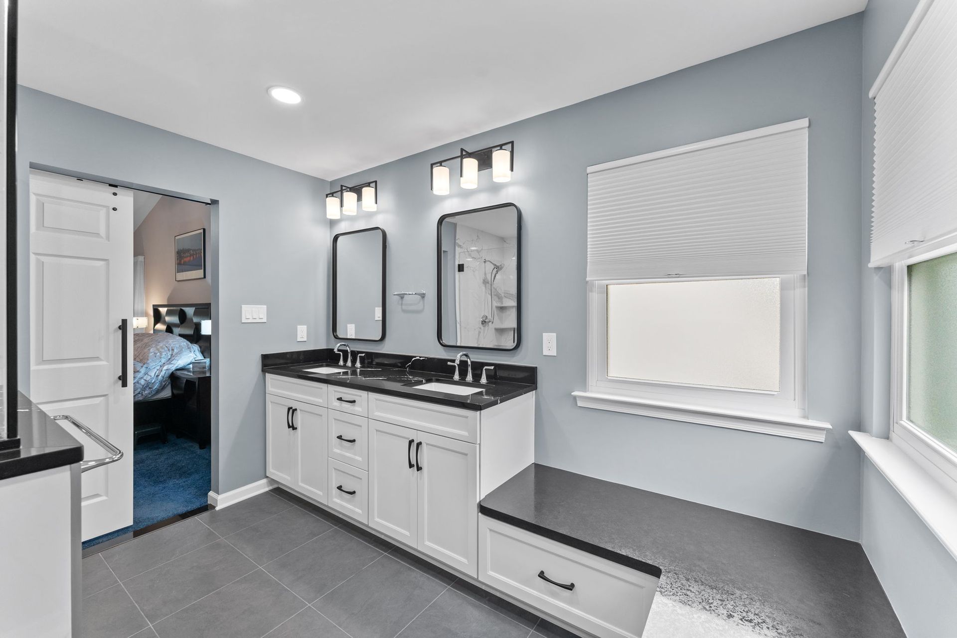 Bright gray bathroom with double vanity, large mirror, and window seat on the right In Bucks County PA