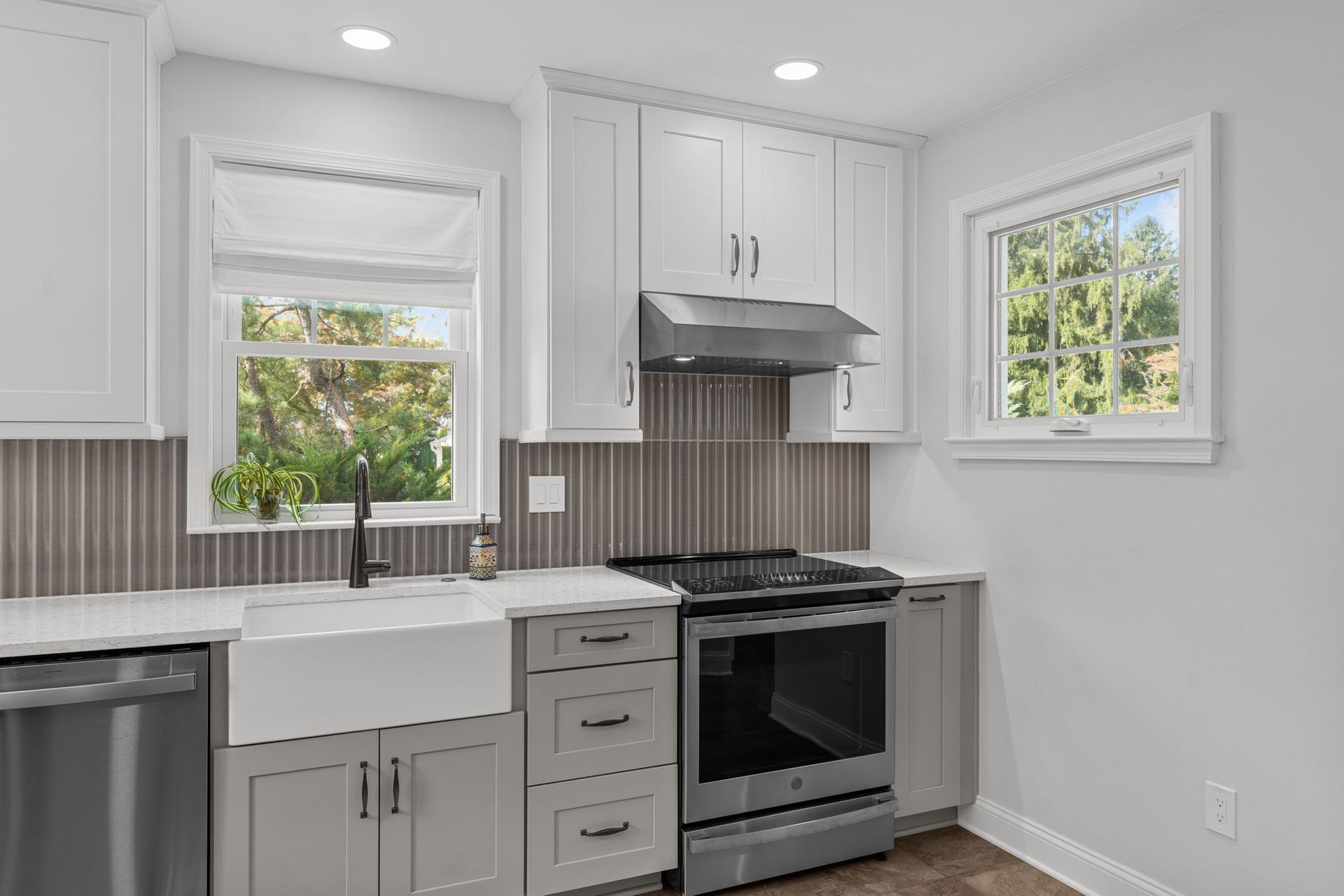 Bright white kitchen with gray cabinets, farmhouse sink, stainless range, and two windows In Bucks County PA