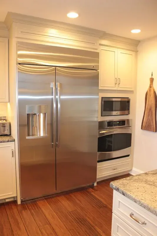 Modern kitchen with stainless steel refrigerator, built-in microwave and oven, wood floor, and granite countertop In Bucks County PA