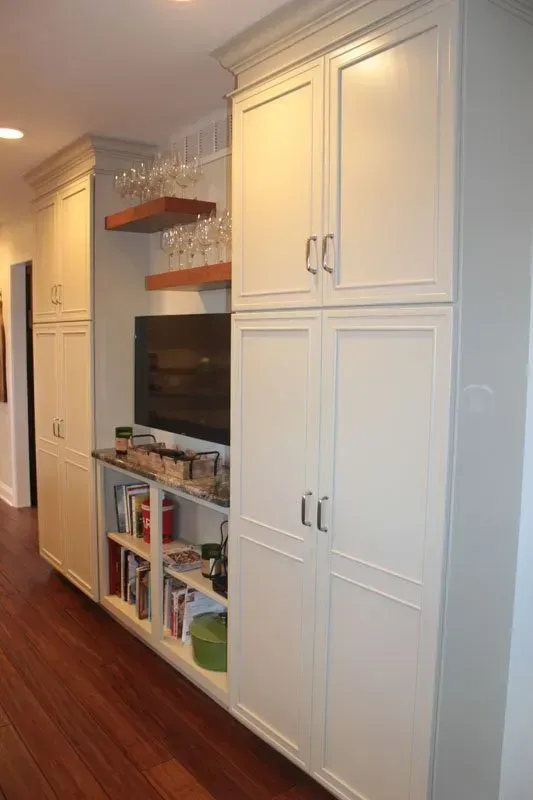 Built-in white cabinets and open shelves beside a TV in a hallway with hardwood floors In Bucks County PA