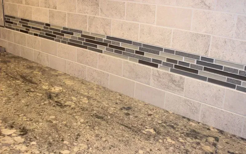 Kitchen countertop with speckled granite and beige tile backsplash with a dark mosaic accent strip In Bucks County PA
