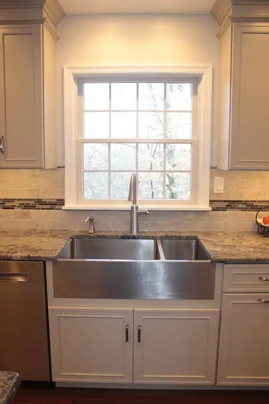 Kitchen sink beneath a window, with granite counters and light-colored cabinets In Bucks County PA