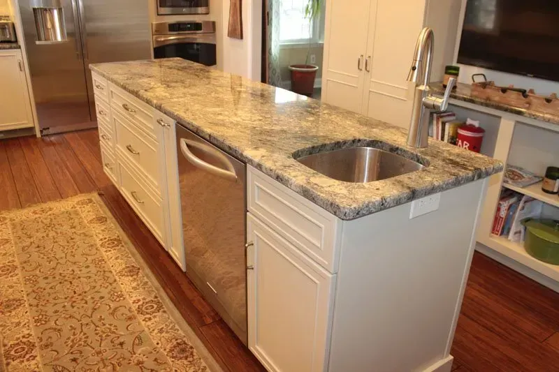 Kitchen island with granite countertop, stainless sink, dishwasher, and patterned runner rug in a bright kitchen In Bucks County PA