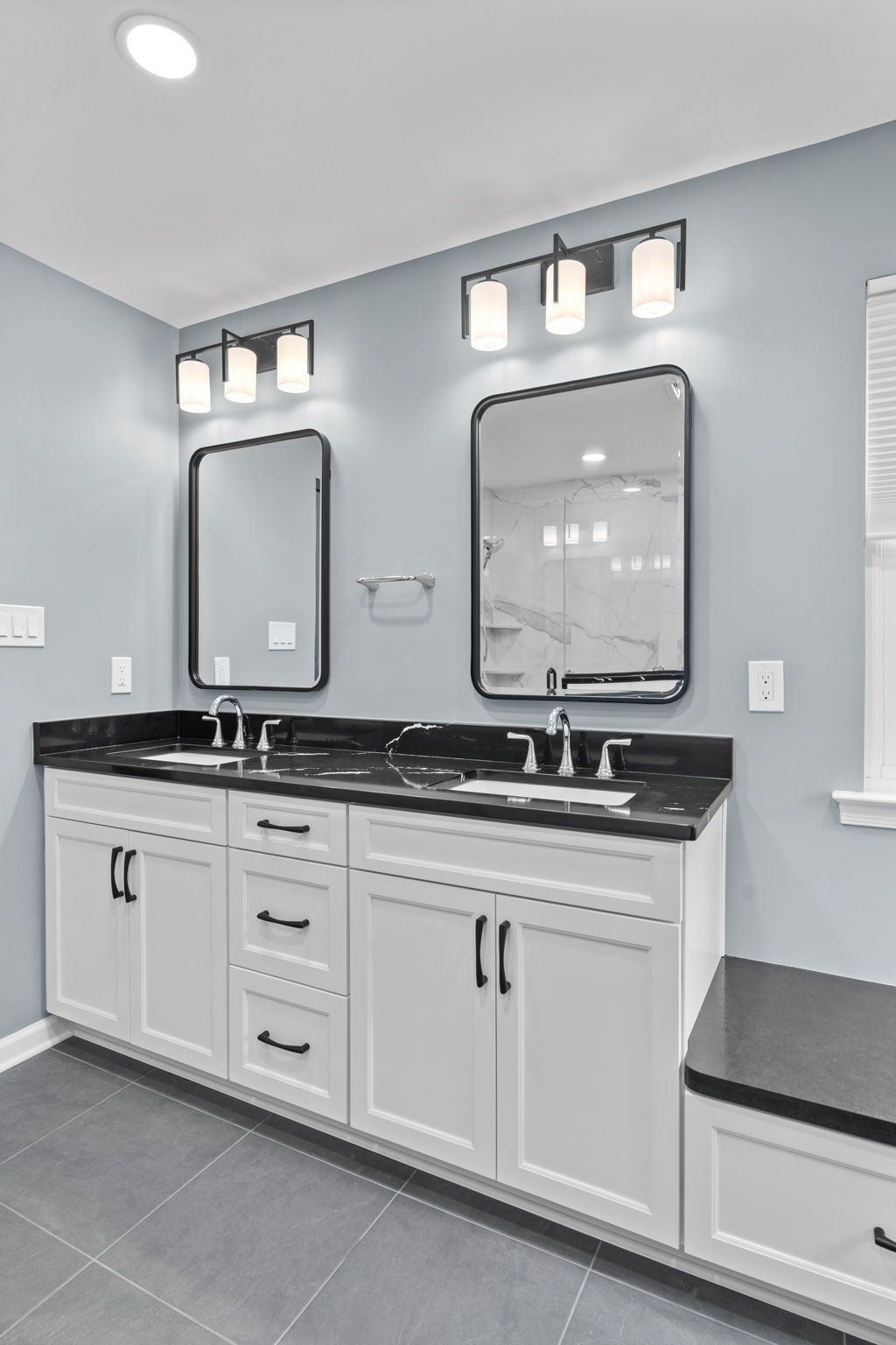 Modern bathroom vanity with double sinks, black countertop, mirrors, and wall sconces on gray walls In Bucks County PA