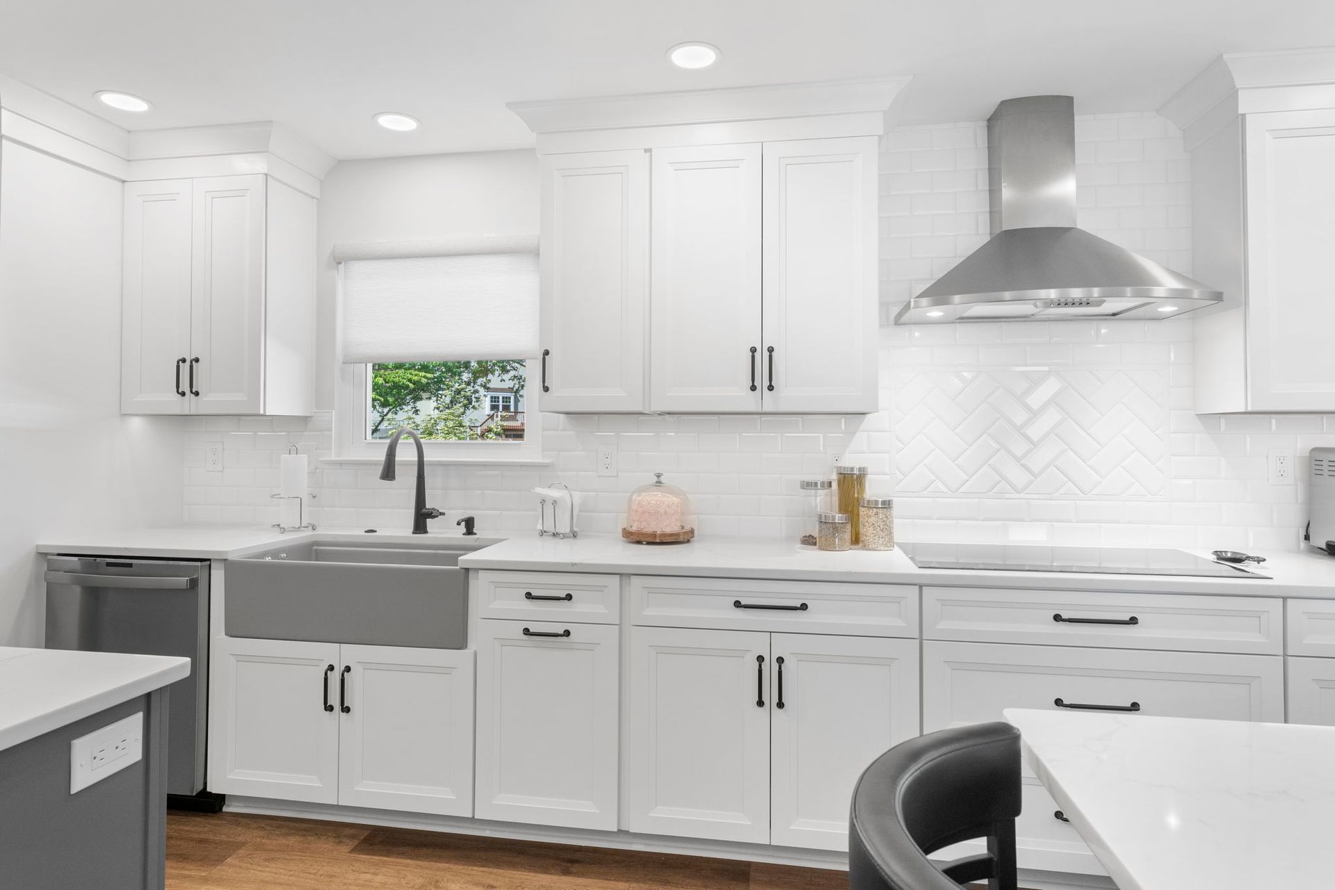 Bright white modern kitchen with gray island, stainless range hood, and window above sink In Bucks County PA