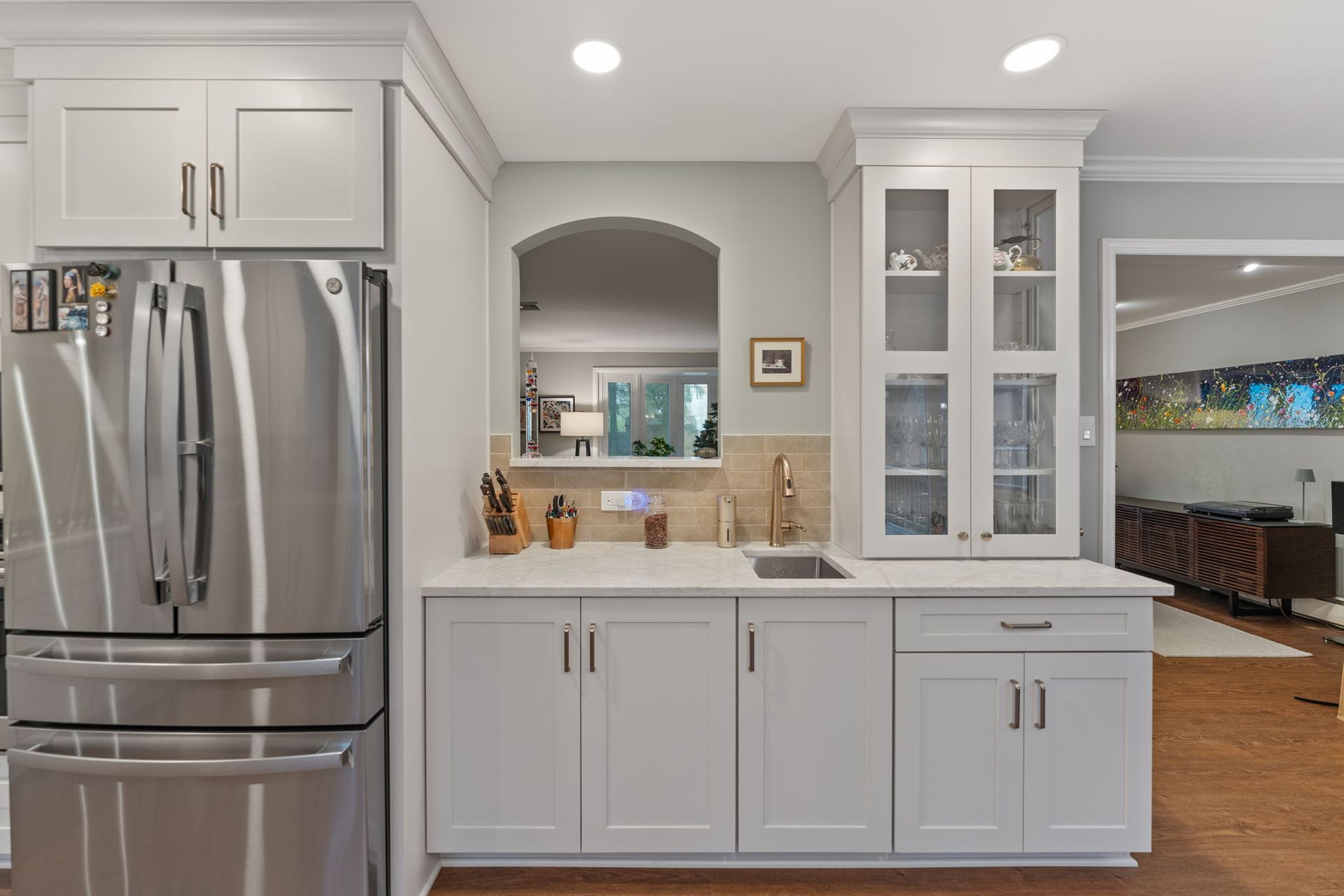 Modern kitchen with stainless steel fridge, white cabinets, and breakfast bar opening to dining area In Bucks County PA