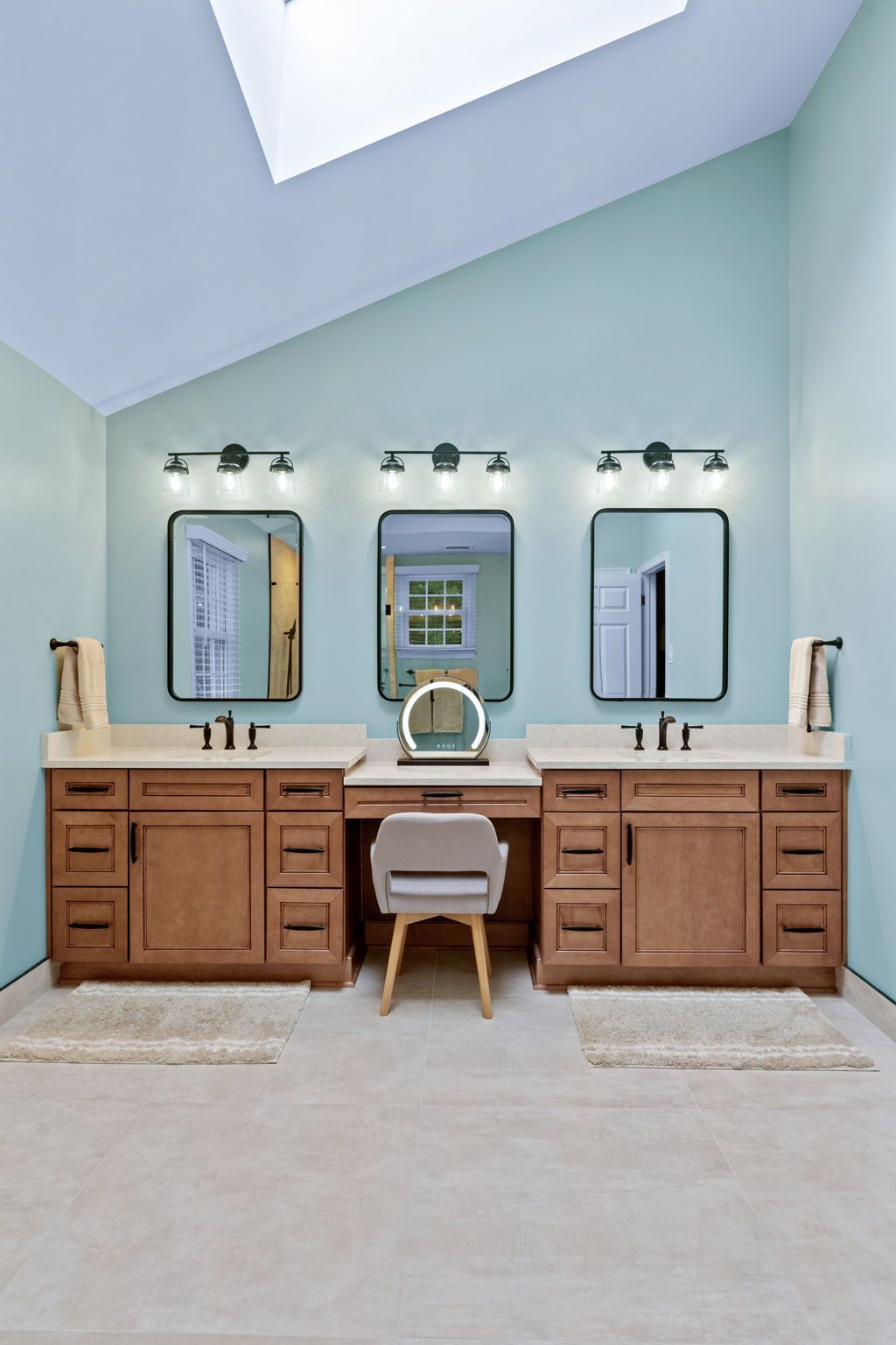 Modern bathroom vanity with three mirrors, light blue walls, and wood cabinets beneath skylights In Bucks County PA