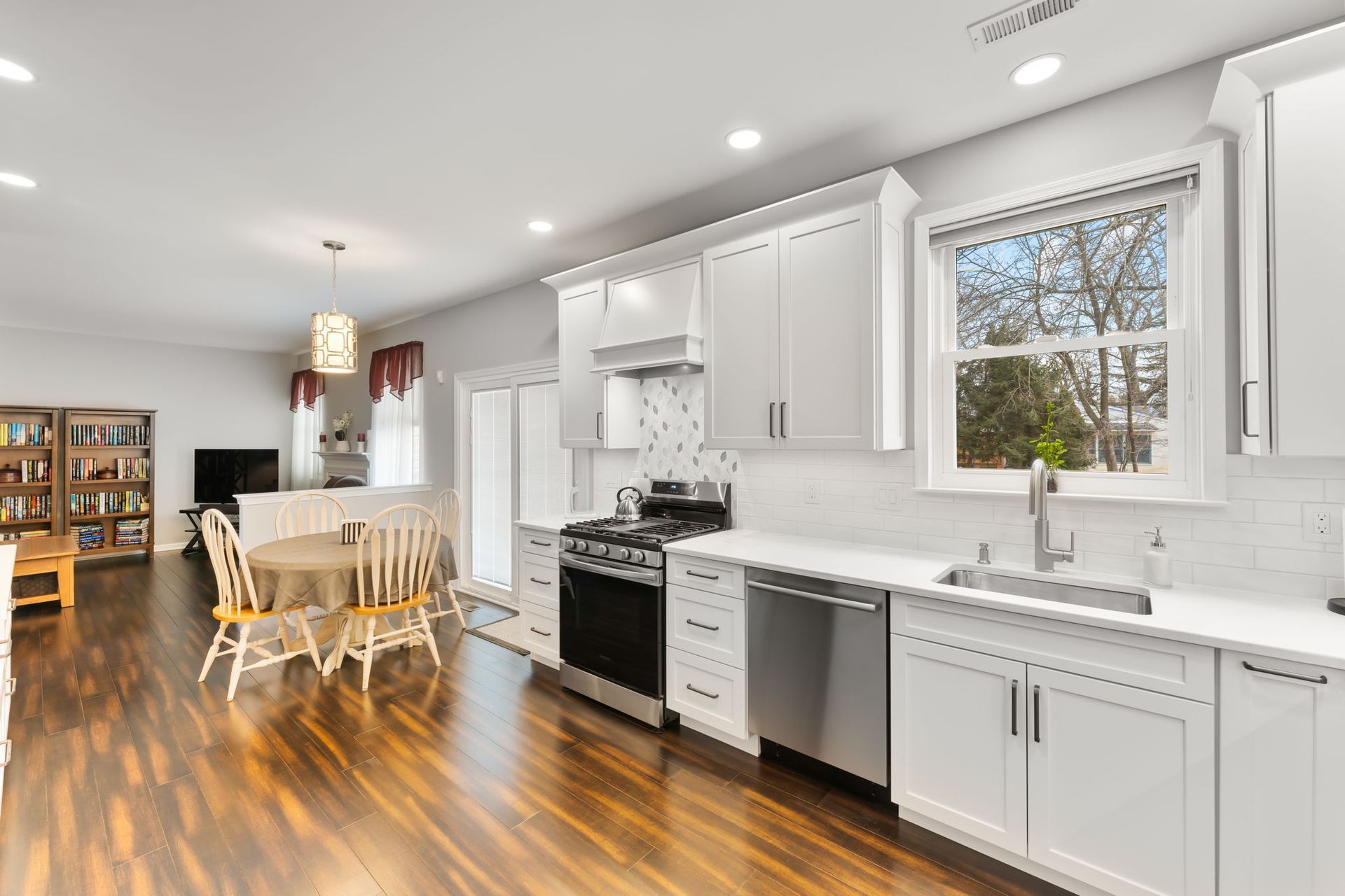 Bright modern kitchen with white cabinets, stainless appliances, wood floor, and a dining table by the window  In Bucks County PA