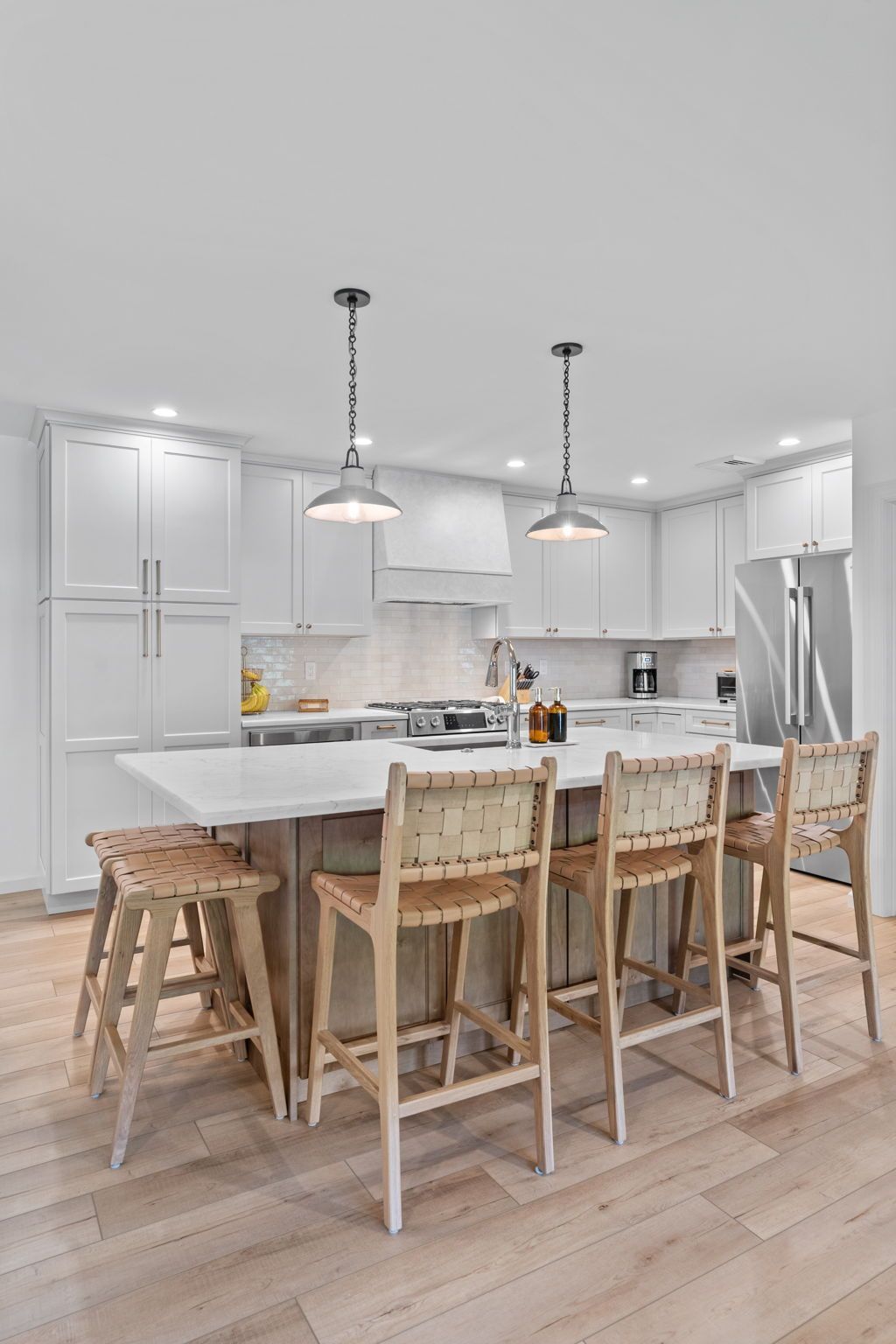 Bright white kitchen with a large island, woven stools, pendant lights, and light wood flooring In Bucks Country PA