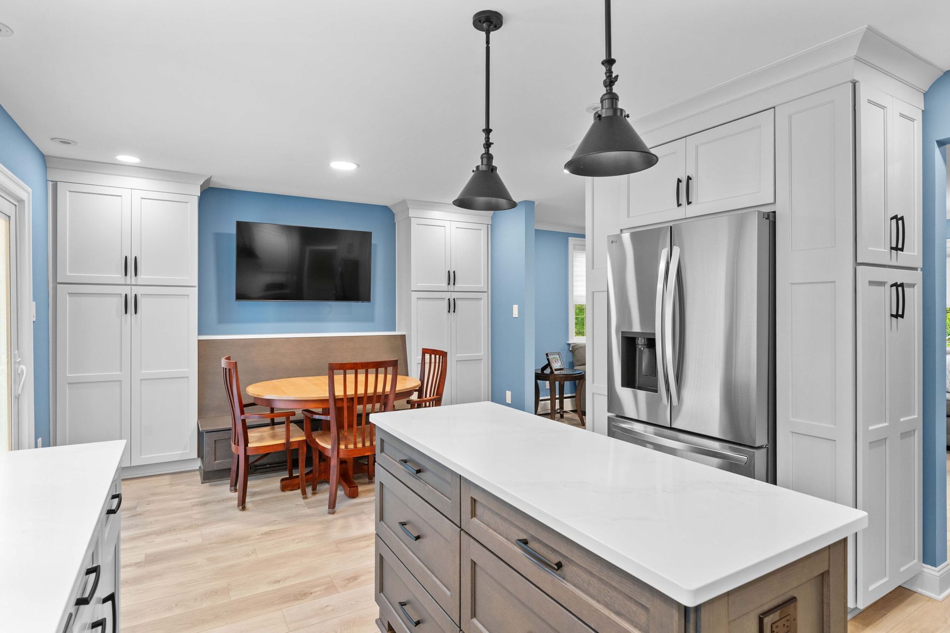 Bright modern kitchen with stainless steel fridge, white cabinets, blue accent wall, and dining table in back in Bucks County PA