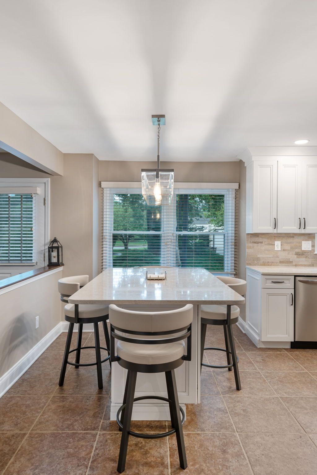Bright kitchen with a white island, three stools, pendant light, and large window In Bucks County PA