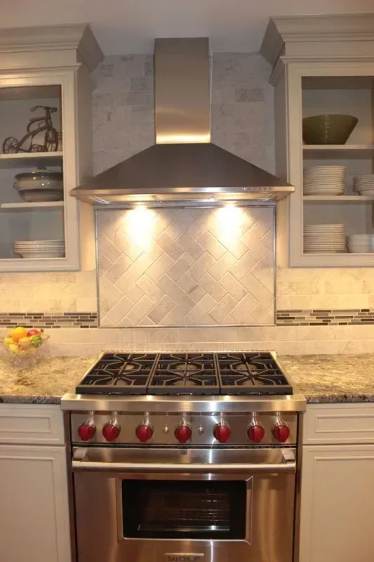 Modern kitchen with stainless steel range, hood, granite countertops, and illuminated tile backsplash In Bucks County PA