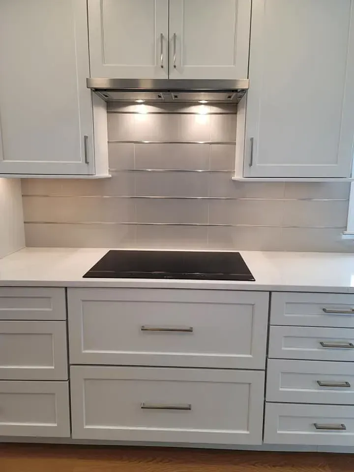 White kitchen with stove, stainless hood, and built-in cabinets around a black cooktop  In Bucks County PA